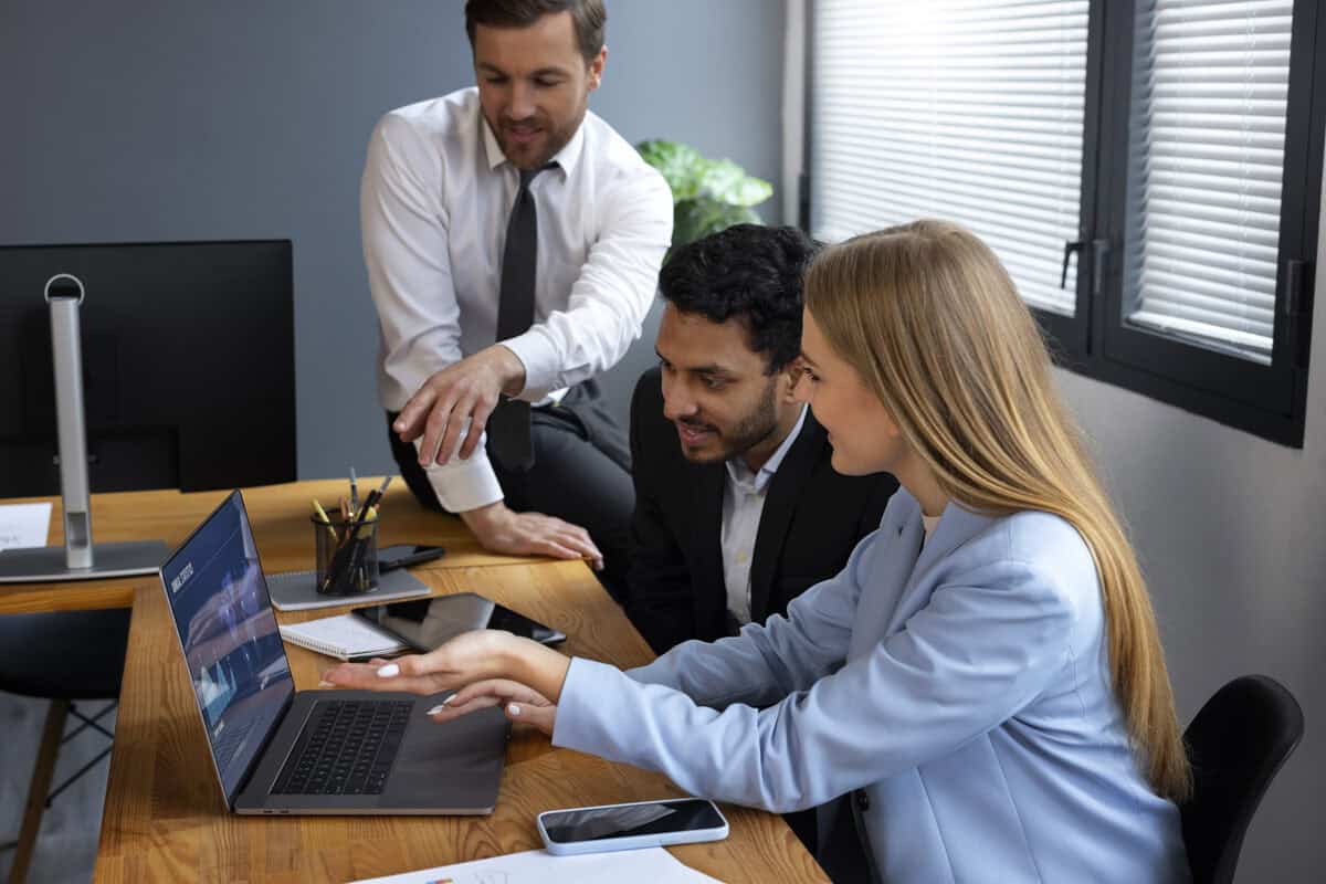 Equipe de vendas de corretora de seguros reunida em torno de um notebook analisando estratégias comerciais