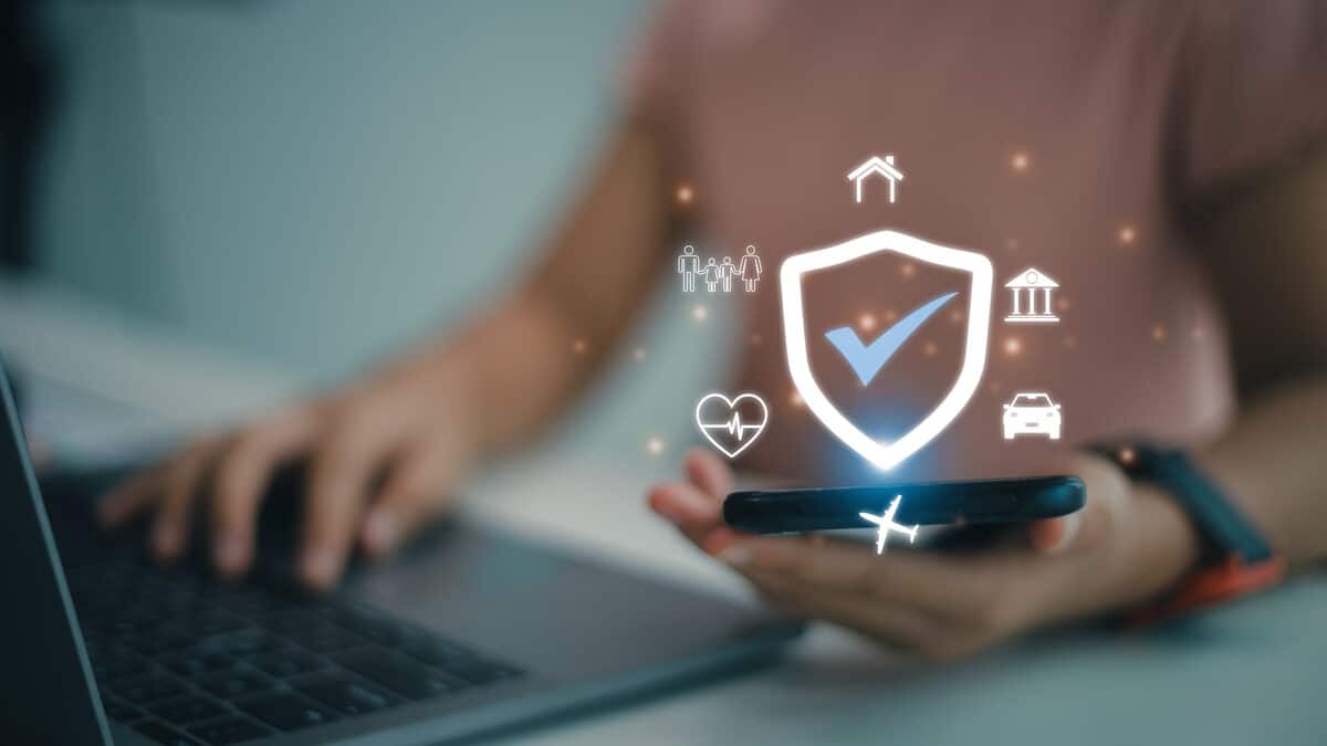 Corretor de seguros usando celular e notebook para gerenciar a renovação de apólices de seguro de clientes