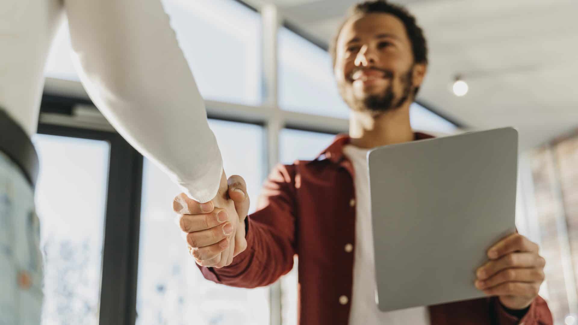 Corretor de seguros cumprimentando cliente ao fechar negócio, ilustrando captação de clientes para corretora