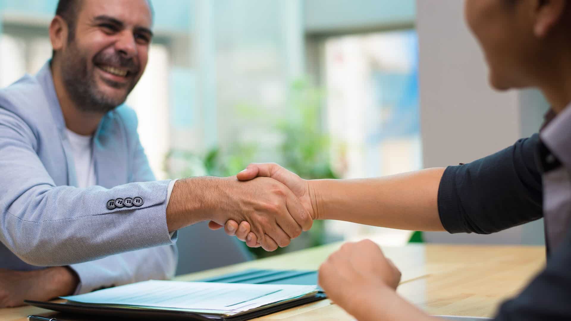 Corretor de seguros e cliente selam acordo com aperto de mão após venda consultiva