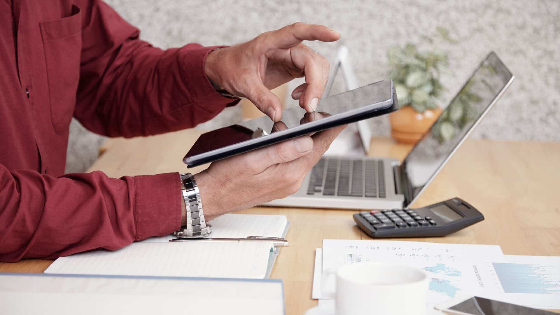 Corretor de seguros usando tablet em mesa com notebook e calculadora para comparar preços e planos da Agger