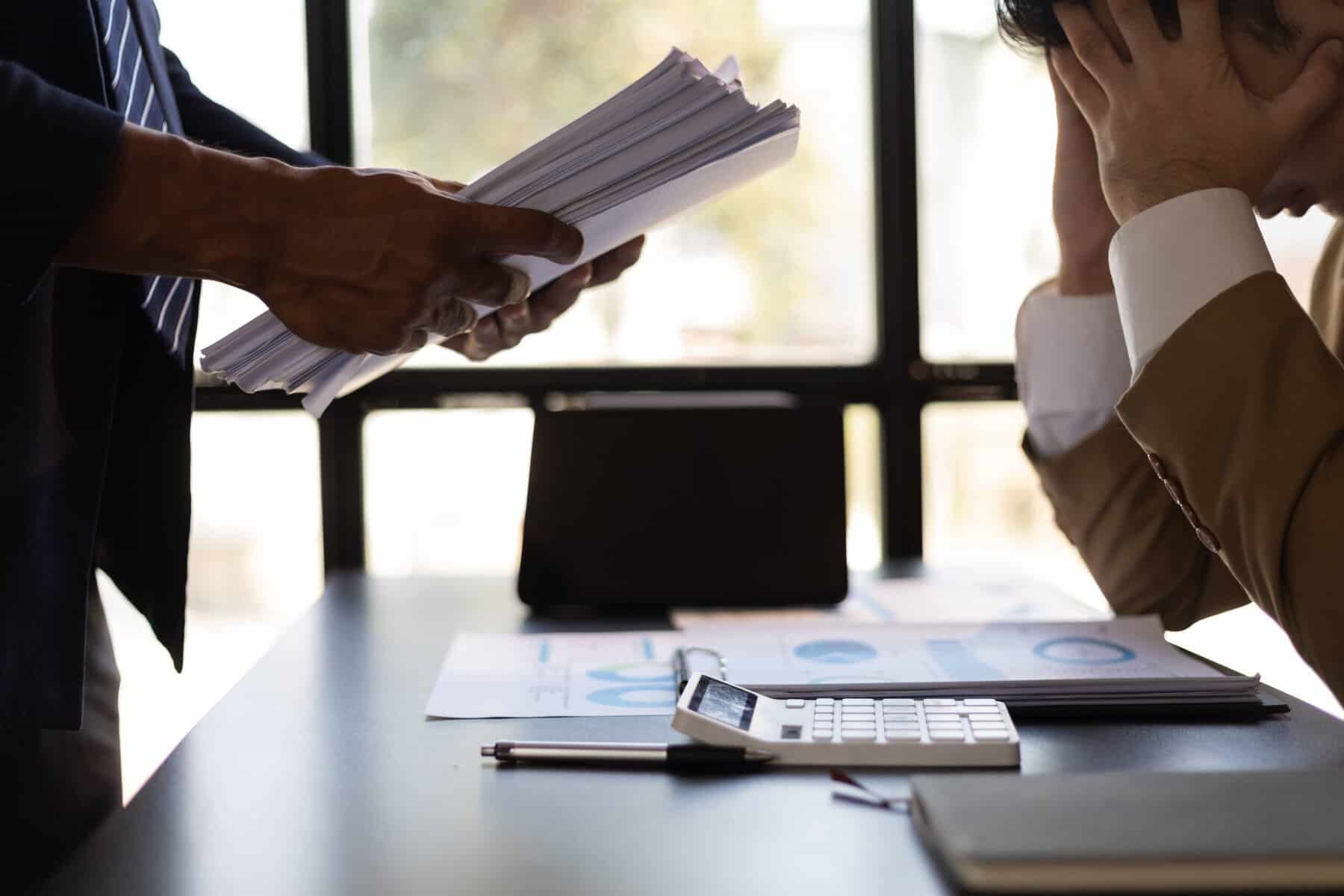 Corretores de seguros extressados, com uma pila de papeis na mão.